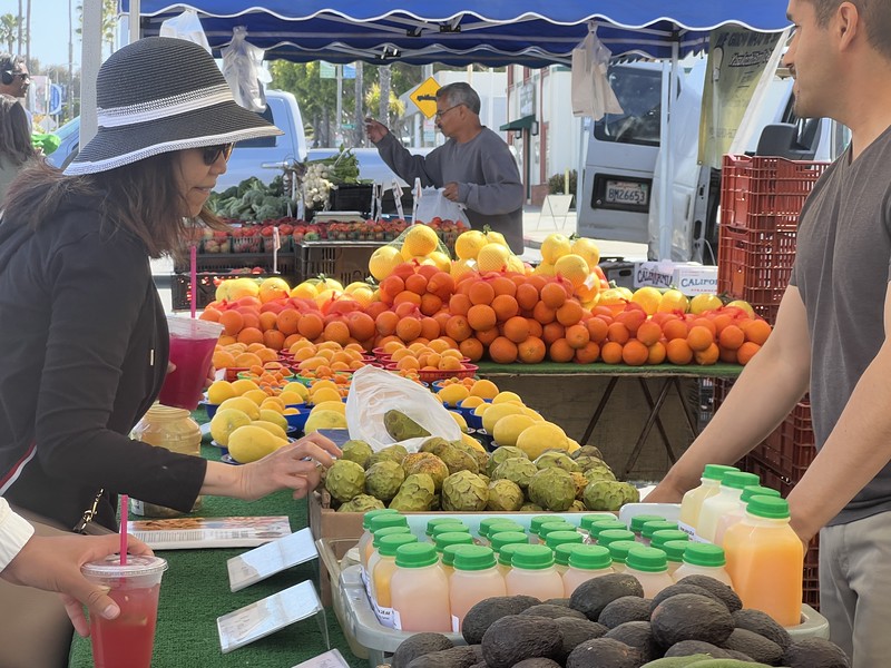 A customer browsing fruit at a certified farmers' market booth