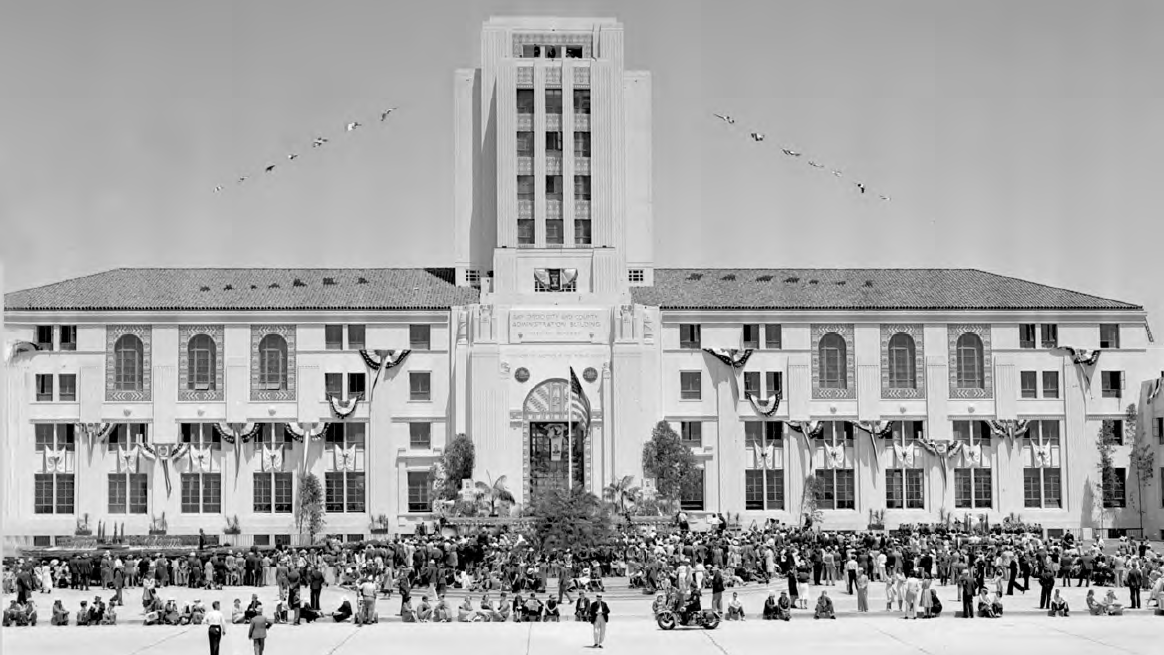 A historical black and white picture of the County Administration Center from the bay looking east with a large group of people gathered in front of the building