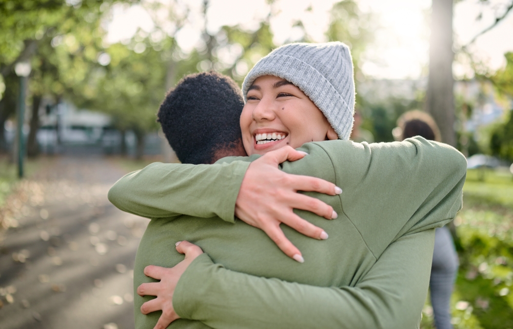 Friends, hug and smile for relationship, support or care embracing love, compassion or friendship in nature. Happy woman and man hugging, smiling and enjoying embrace in happiness for partnership