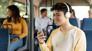 Teen boy on bus with headphones and looking at cell phone