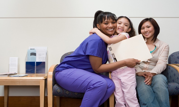 CCS / Shutterstock Image Stock photo of a nurse in an office, hugging a child that is standing near her mother.