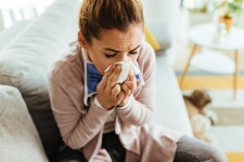 Young ill woman sneezing in a tissue at home.