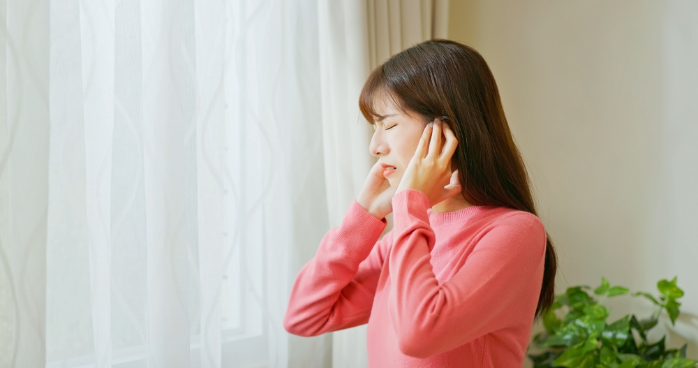 asian woman feel annoyed and she is suffering noise from outside at home - trying covering her ears
