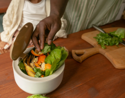Individuals composting food waste in a small bin on the table.
