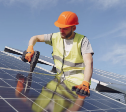 Individual wearing a hard hat and installing a rooftop solar panel system.