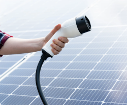 Individual holding an electric vehicle charger in front of a solar panel.