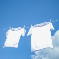 Two White Shirts Air Drying with a Blue Sky and Clouds in Backyard