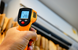 Individual pointing an infrared thermometer to an air conditioner